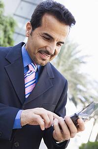 Businessman outdoors using personal digital assistant and smiling (high key/selective focus)