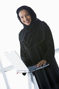 Woman indoors standing with laptop and smiling (high key/selective focus)