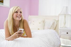 Teenage Girl Lying On Bed Using Mp3 Player