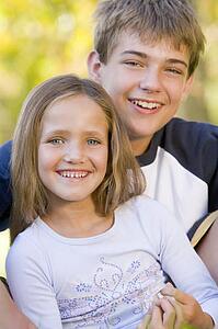 Brother and sister sitting outdoors smiling