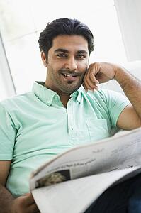 Man in living room with newspaper smiling (high key/selective focus)