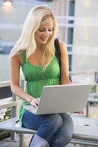 Woman sitting on bench outdoors with laptop smiling (selective focus)
