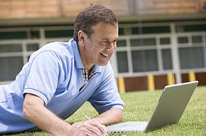 Man lying on lawn of school with laptop