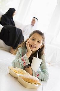 Young girl with fast food in living room smiling with parents in background (high key/selective focus)