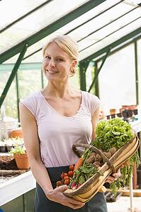 Woman in greenhouse holding basket of vegetables smiling