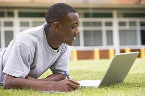 Student lying outdoors on lawn with laptop