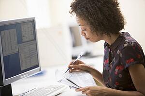 Woman in computer roon circling items in newspaper