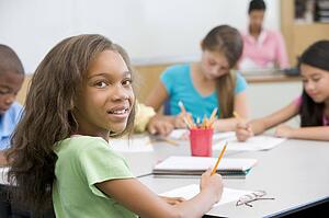 Students in class writing with teacher in background (selective focus)