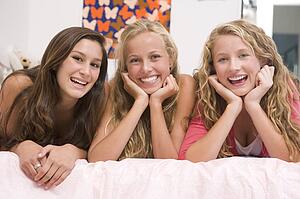 Teenage Girls Lying On Bed Using Mobile Phone