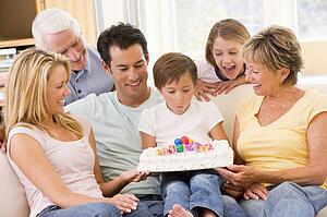 Family in living room smiling with young boy blowing out candles on cake