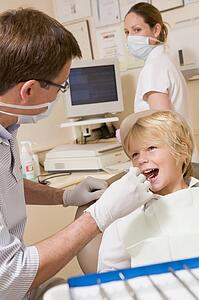 Dentist and assistant in exam room with young boy in chair