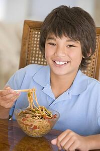 Young boy in dining room eating chinese food smiling