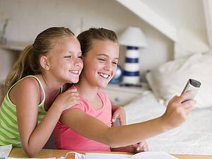 Young Girls Distracted From Their Homework, Playing With A Cellphone