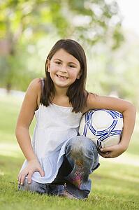 Young girl outdoors at park holding ball and smiling (selective focus)