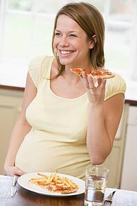 Pregnant woman in kitchen eating French fries and pizza smiling