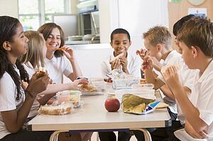 Students sitting at cafeteria table eating lunch (depth of field)