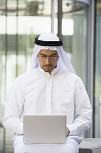 Businessman sitting outdoors with laptop by building (selective focus)
