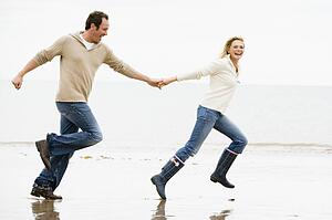 Couple running on beach holding hands smiling