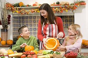 Mother and two children carving jack o lanterns on Halloween and smiling