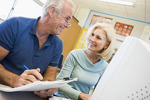 Two people at computer terminal with notepad