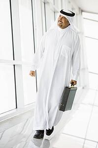 Businessman walking in a corridor with a briefcase smiling (high key/selective focus)