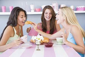 Three young woman sitting at a table having tea and a snack
