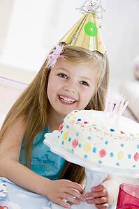 Young girl wearing party hat with birthday cake smiling