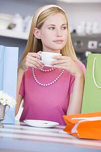 Young woman sitting at a table taking a break from shopping and drinking tea