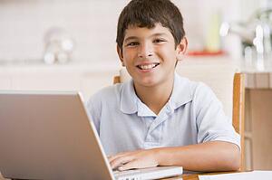 Young boy in kitchen with laptop and paperwork smiling
