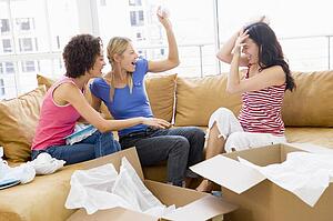 Three girl friends playfully unpacking boxes in new home smiling