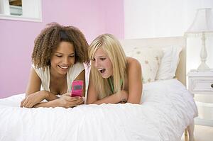 Teenage Girls Lying On Bed Using Cellphone 