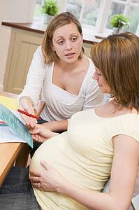 Pregnant woman in kitchen with friend reading pamphlet