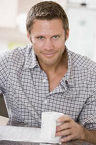 Man in kitchen reading newspaper and smiling