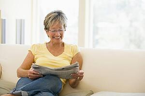 Woman relaxing with newspaper in living room smiling