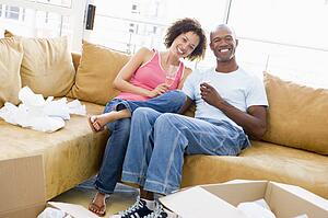 Couple relaxing with champagne by boxes in new home smiling