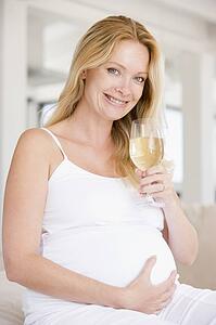 Pregnant woman with glass of white wine smiling