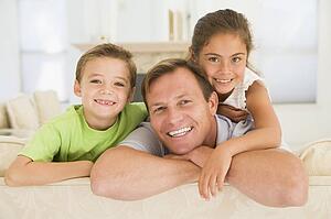 Man and two young children sitting in living room smiling