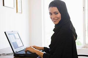 Woman in office with laptop smiling (high key/selective focus)