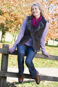Woman outdoors sitting on fence smiling (selective focus)