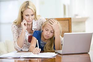Woman helping young girl with laptop do homework in dining room