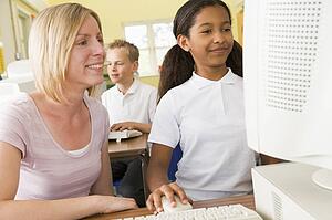 Student and teacher at computer terminal with student in background
