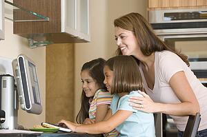 Woman and two young girls in kitchen with computer smiling