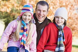 Father and two young children outdoors in park smiling (selective focus)