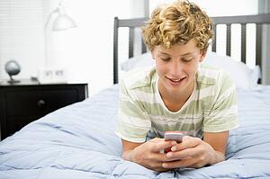 Teenage Boy Lying On Bed Using Mobile Phone 