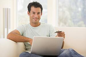 Man in living room using laptop and holding credit card smiling