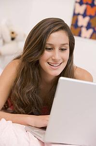 Teenage Girl Lying On Her Bed Using Laptop
