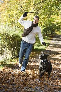 Man outdoors with dog on path in park holding branch smiling (selective focus)