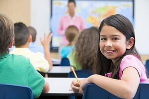 Student in class looking at camera with teacher in background (selective focus)