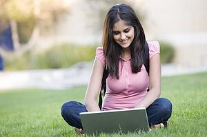 Woman outdoors sitting on grass with laptop (selective focus)