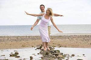 Couple at the beach walking on stones and smiling
